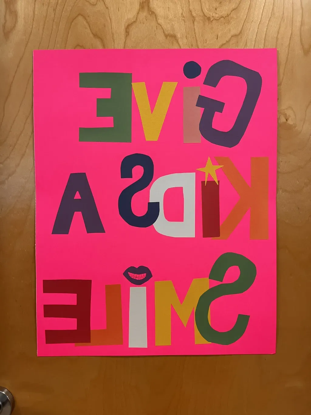 A pink poster against a wooden door reads "Give Kids a Smile"