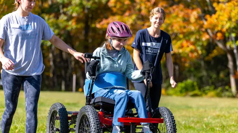 UNE volunteers assist a power soccer player outside