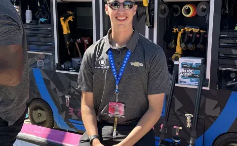 A UNE student sits on the edge of a race track pit wearing sunglasses