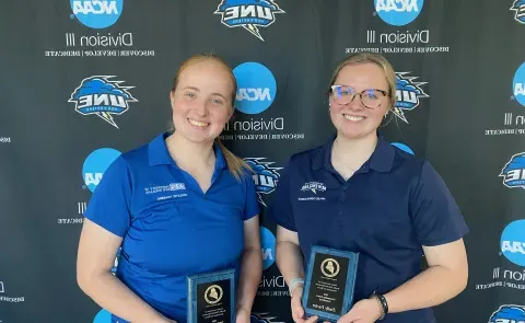 Two female students pose for a photo holding awards